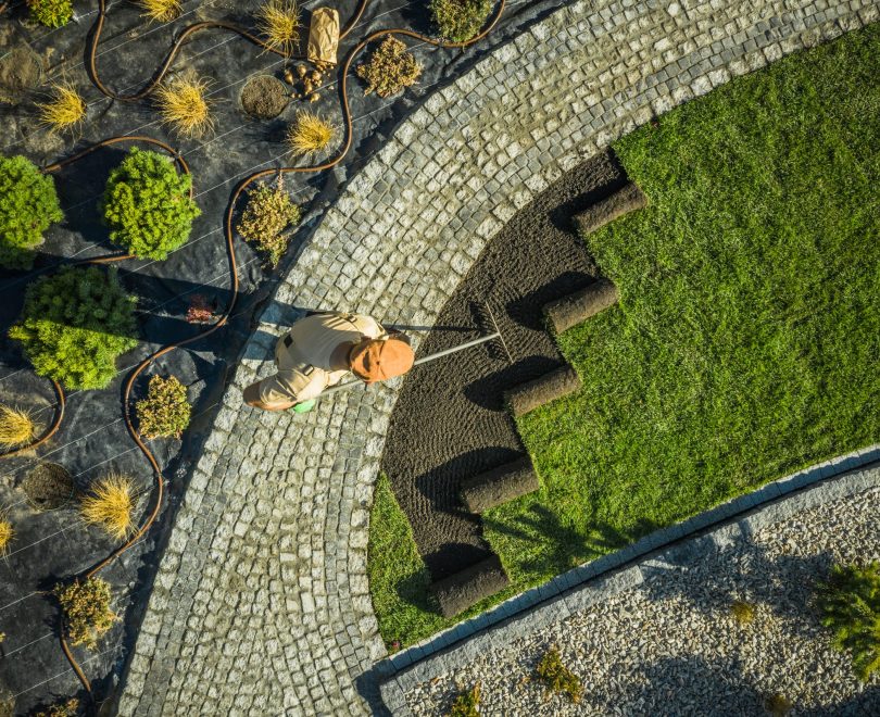 Gardener in Newly Build Backyard Garden Installing Natural Grass Turfs. Preparing Soil. Aerial View.