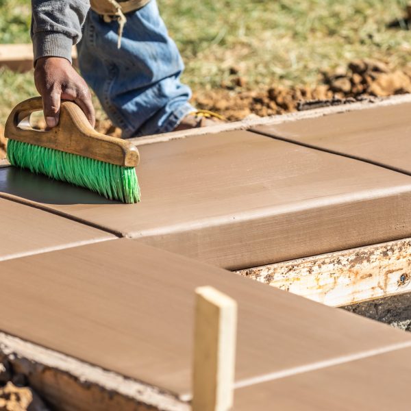 Construction Worker Using Brush On Wet Cement Forming Coping Around New Pool.