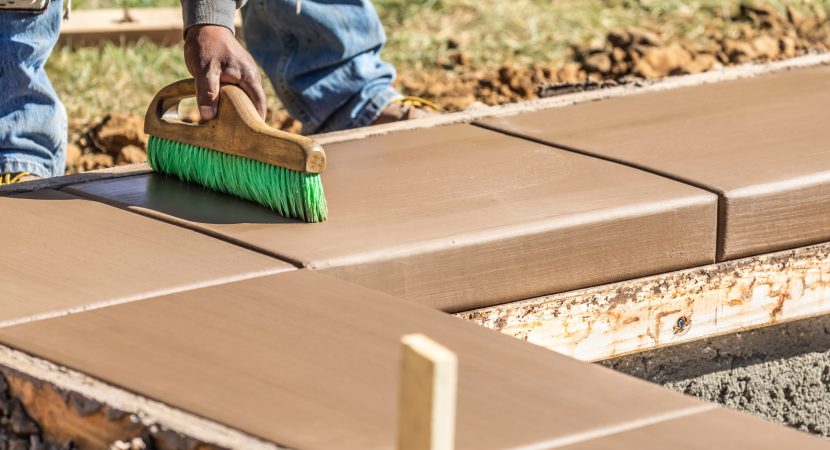 Construction Worker Using Brush On Wet Cement Forming Coping Around New Pool.