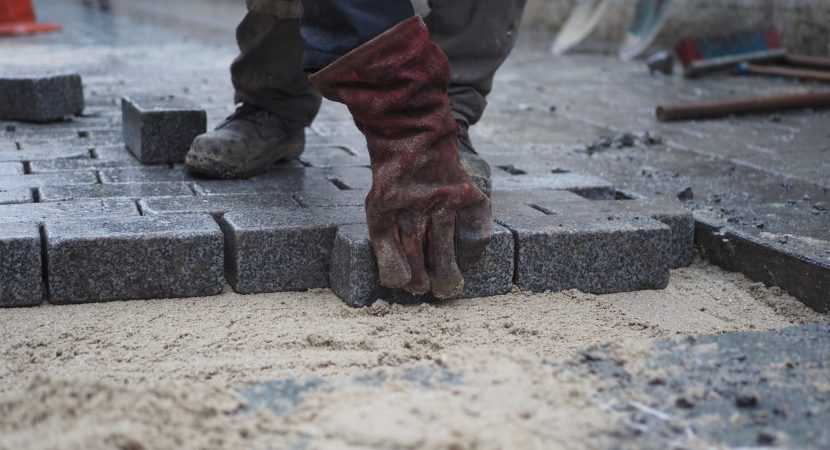 A skilled laborer is expertly placing stone pavers meticulously on a busy construction job site