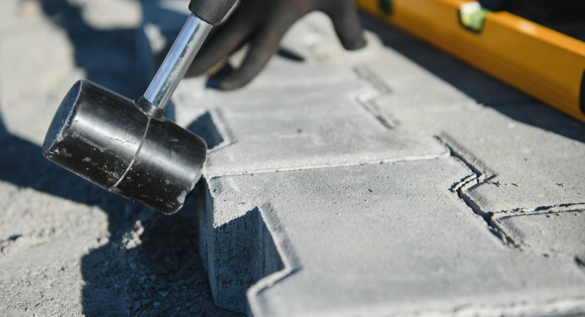 Builder laying a paving brick placing it on the sand foundation with gloved hands.